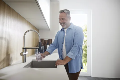 Mann zapft gefiltertes Wasser direkt an der Küchenarmatur in ein Glas