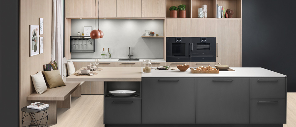 Küche mit dunklen oder holzfarbenen Fronten, heller Arbeitsfläche, dunklen Einbaugeräten und integriertem Sitzbereich